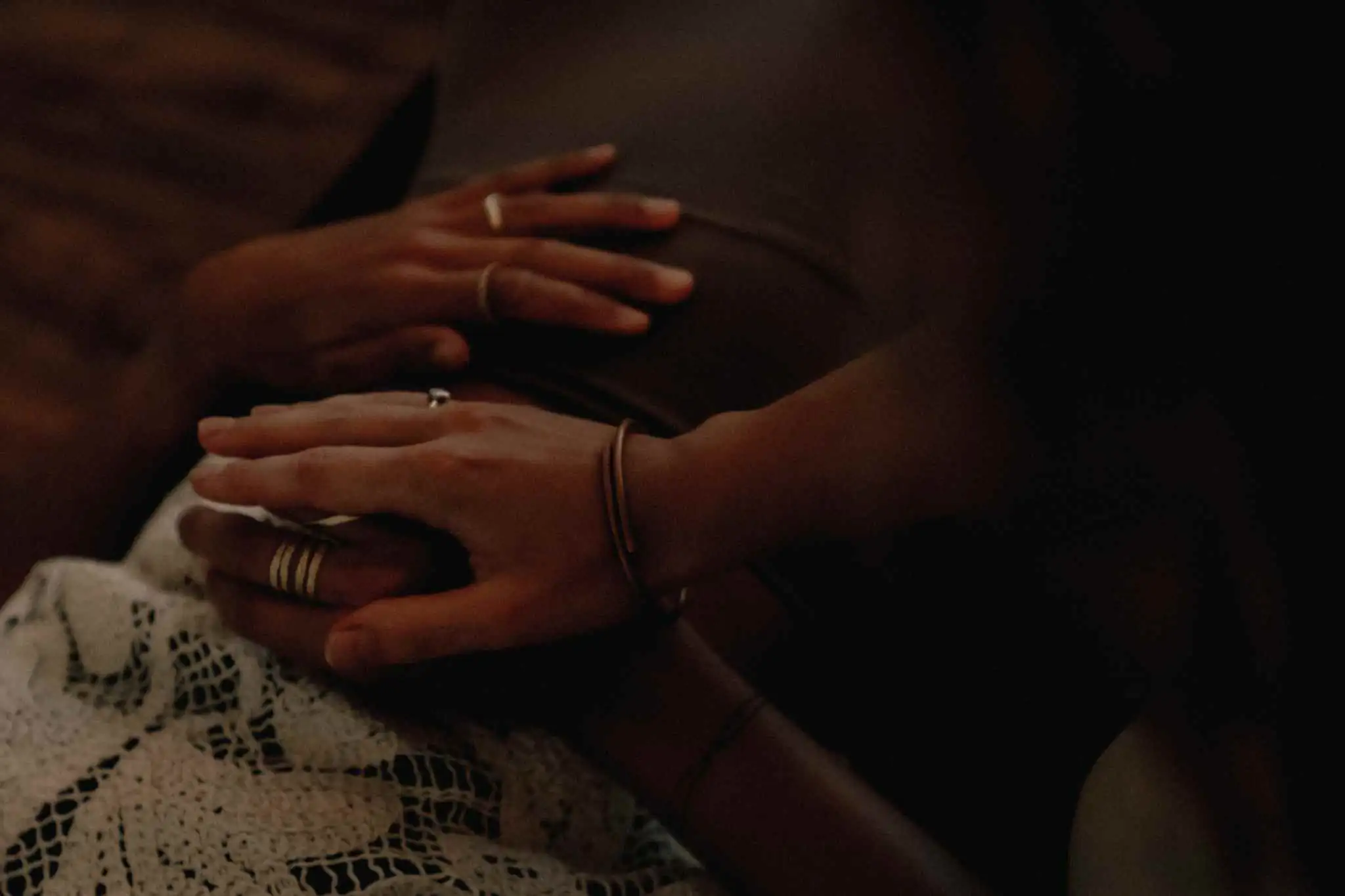 A close-up in low light of two pairs of hands resting on the chest of someone lying down during a breathwork session