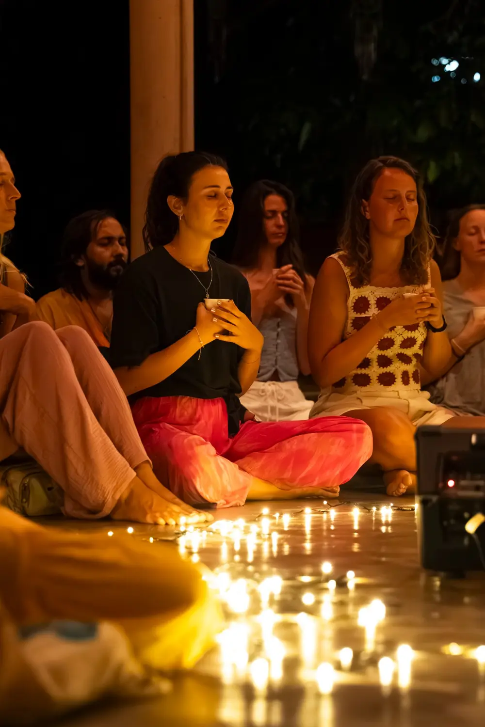 Guests holding cups of Caorā cacao in a candlelit circle at a Senses event