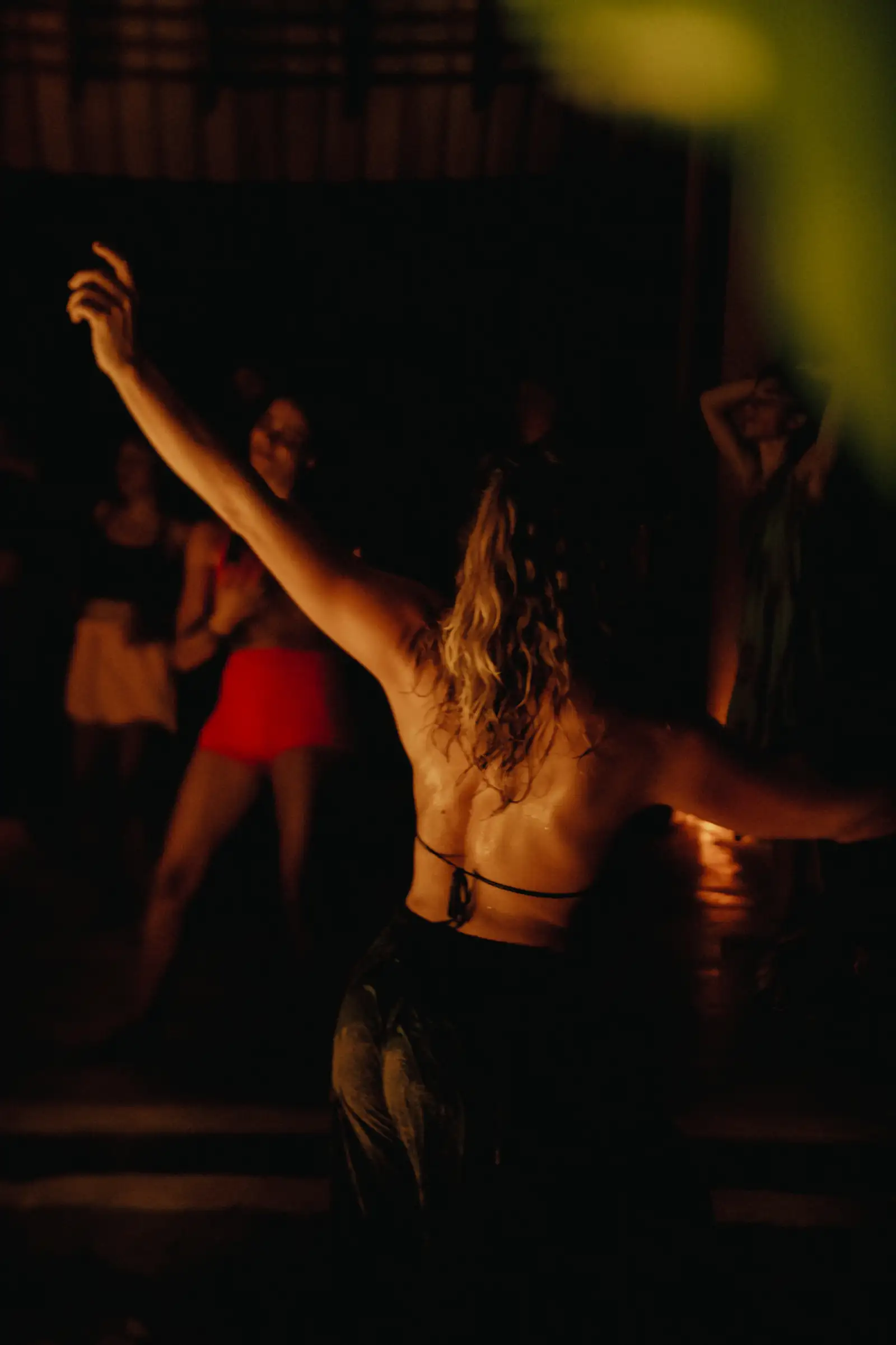 A dancer with arms raised, seen from behind, at a night-time ecstatic dance in warm light at Senses