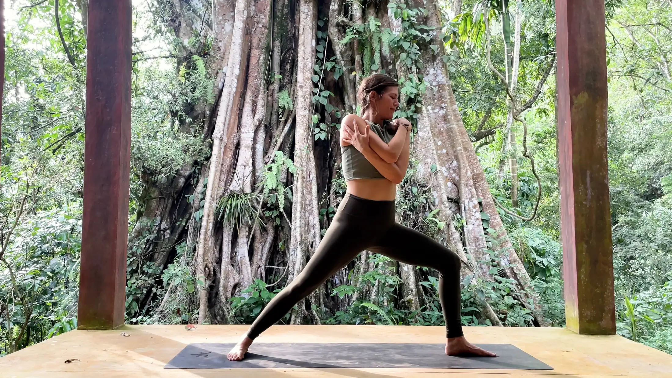 Elena Orth in a standing lunge on a wooden deck before a large banyan tree and dense green jungle at Senses Sri Lanka