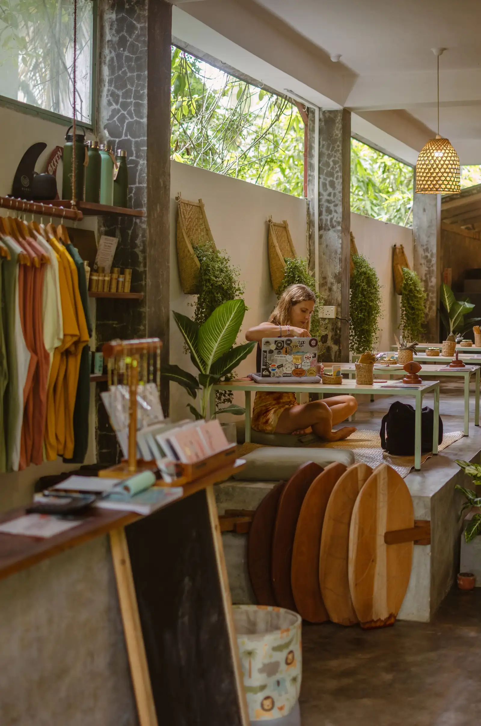 The plant filled interior of Flow Café, Weligama, with a rack of clothes, wooden bellyboards and mint green tables