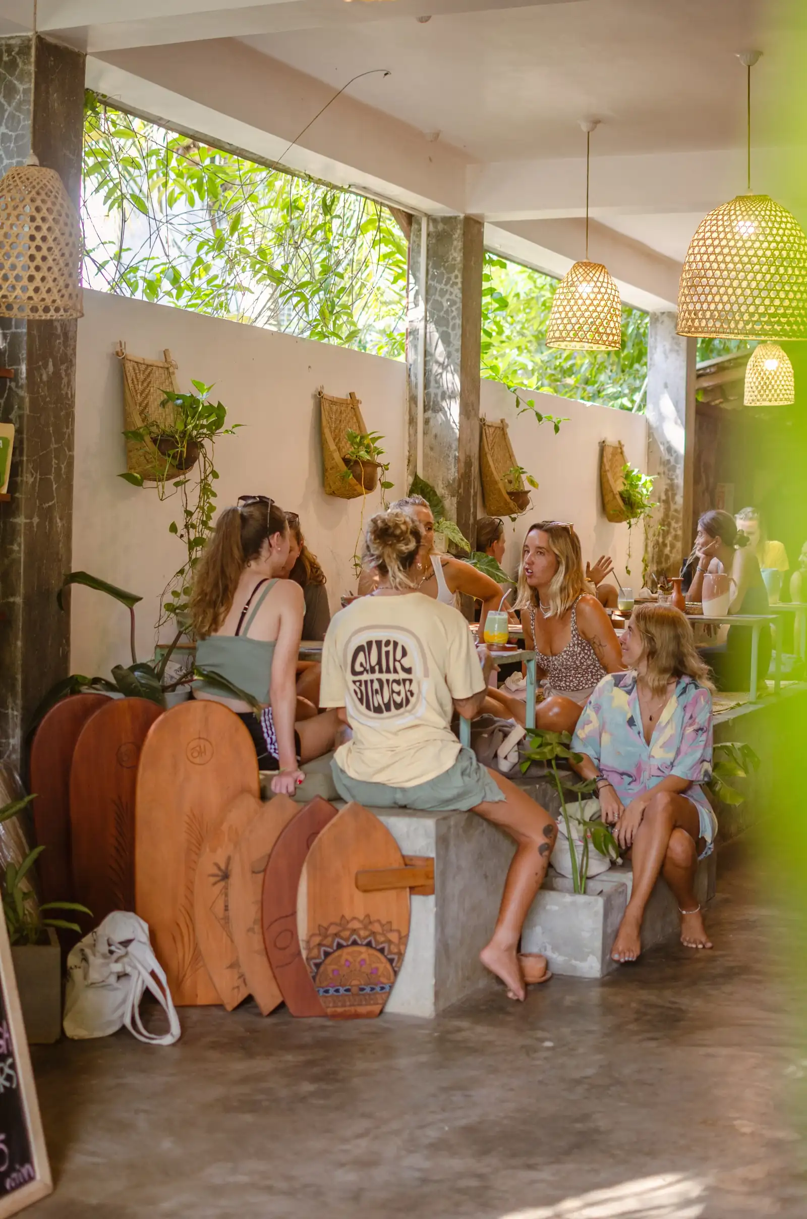 People sitting and talking on surfboard backed seating against a plant wall at Flow Café, Weligama